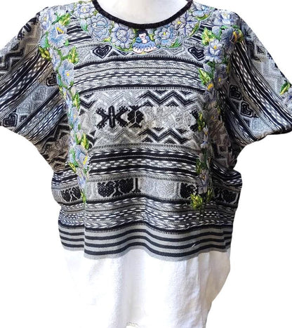 May include: A gray and black embroidered top with a white bottom. The top features intricate patterns, including floral and geometric designs. The neckline is black, and the sleeves are short. The bottom portion is a plain white fabric.