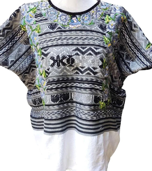May include: A gray and black embroidered top with a white bottom. The top features intricate patterns, including floral and geometric designs. The neckline is black, and the sleeves are short. The bottom portion is a plain white fabric.