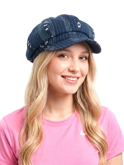 May include: A navy blue newsboy cap featuring a subtle white pinstripe pattern and small, scattered white and teal geometric motifs. The hat has a rounded, multi-paneled crown and a short, stiff brim, constructed from a textured fabric.